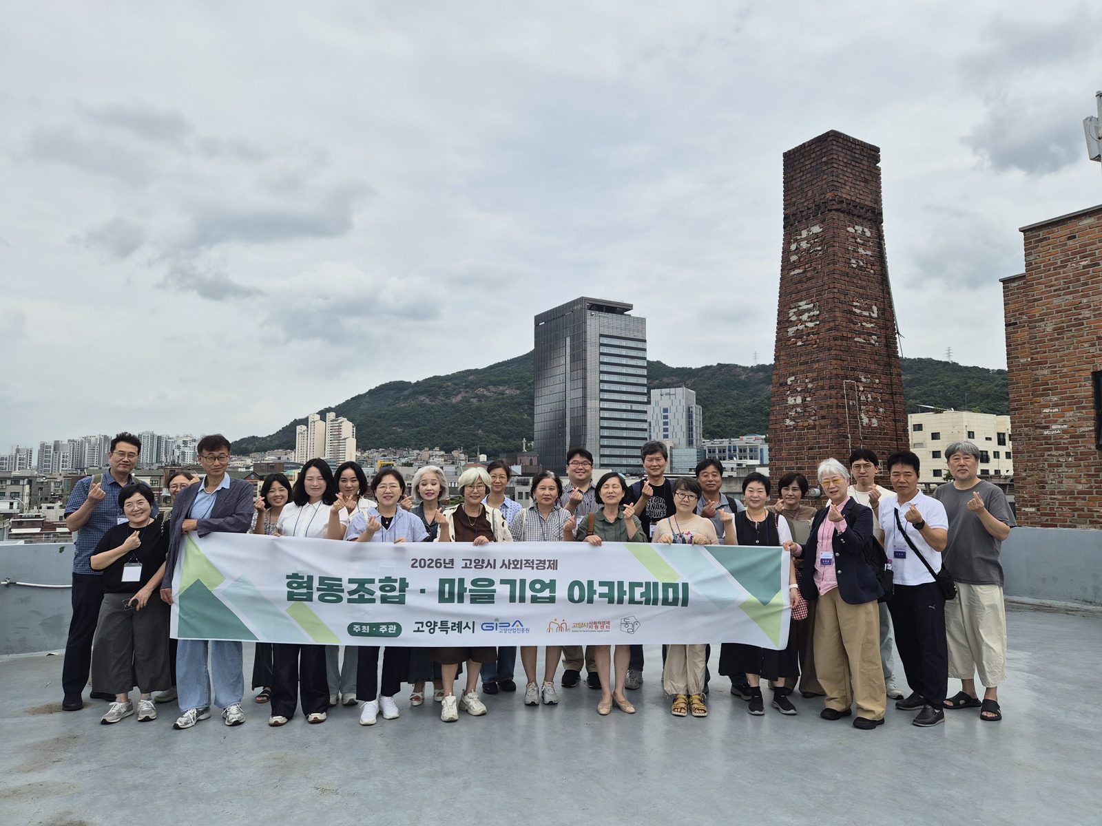 광사넷 옥상에서 고양시사회적경제연합회 탐방단이 협동조합·마을기업 아카데미 현수막을 들고 찍은 단체사진