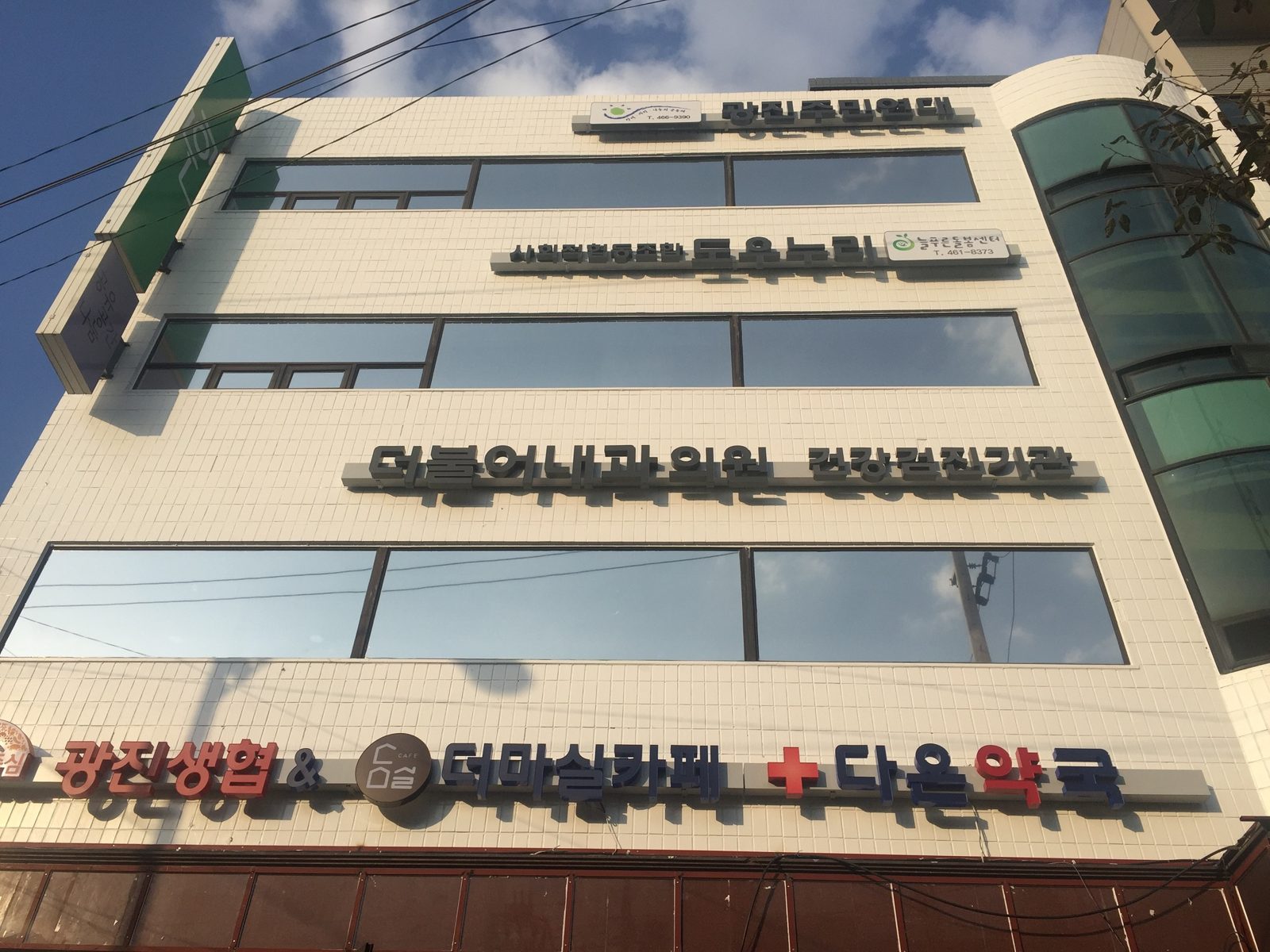 아래에서 올려다본 층별 간판: 광진주민연대, 도우누리·늘푸른돌봄센터, 더불어내과의원, 광진생협·더마실카페·다온약국